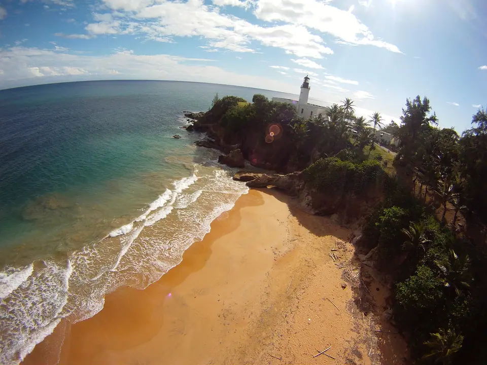 Aerial view of the white Punta Tuna lighthouse on a green headland above the sea in Maunabo