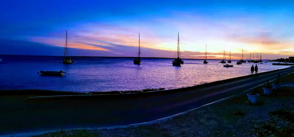Sailboats at anchor off the Kralendijk waterfront boulevard on Bonaire at dusk under a purple sky