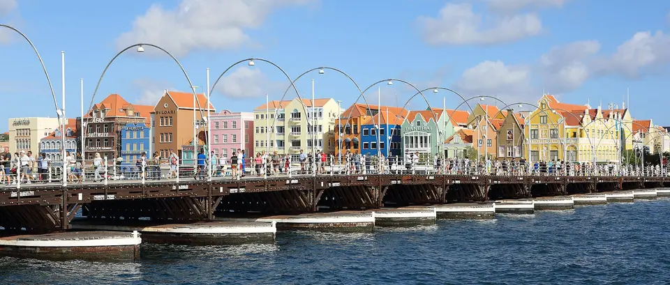 The Queen Emma pontoon bridge with arched lights crossing the harbor to the colorful Handelskade buildings in Willemstad