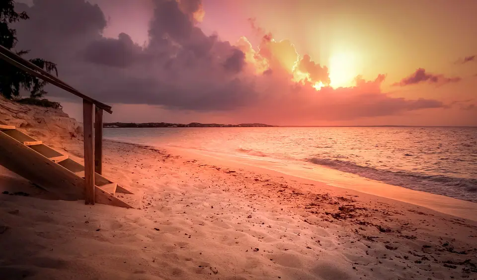 Pink and orange sunset sky over the calm water and sand of Grace Bay, with wooden beach steps in the foreground