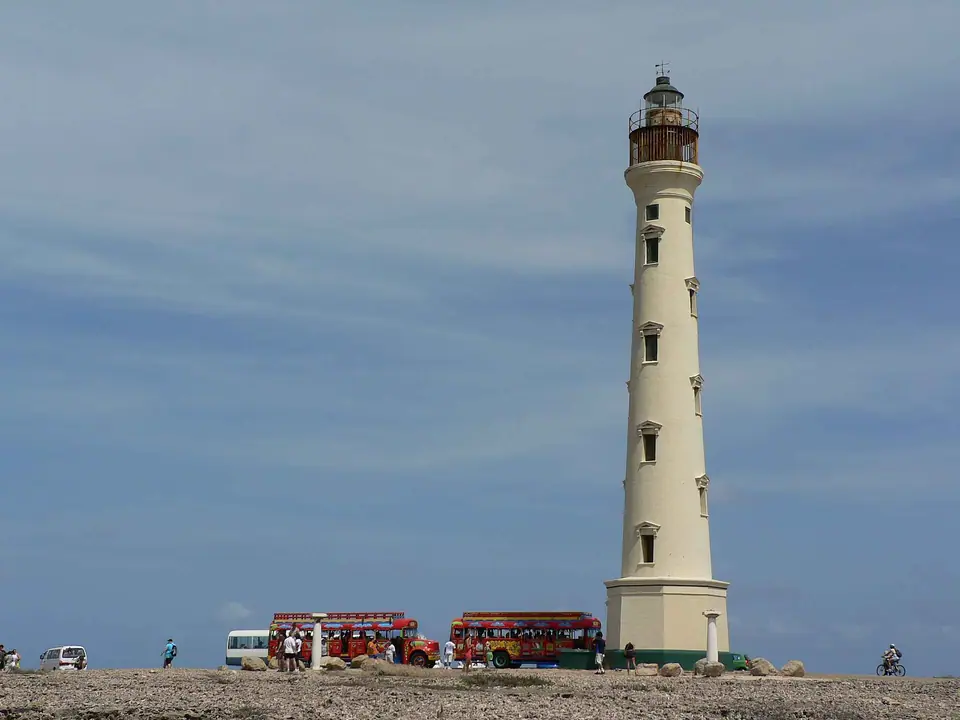 The tall white California Lighthouse on Aruba's northwest tip, with tour vehicles parked at its base