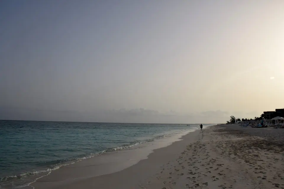 Long empty stretch of Grace Bay beach at dusk with gentle waves and a lone walker in the distance