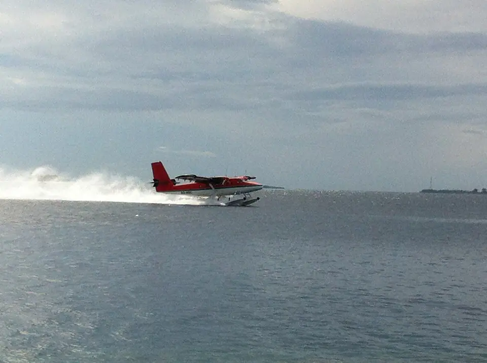 Floatplane taxiing on turquoise water beside a resort jetty in the Maldives
