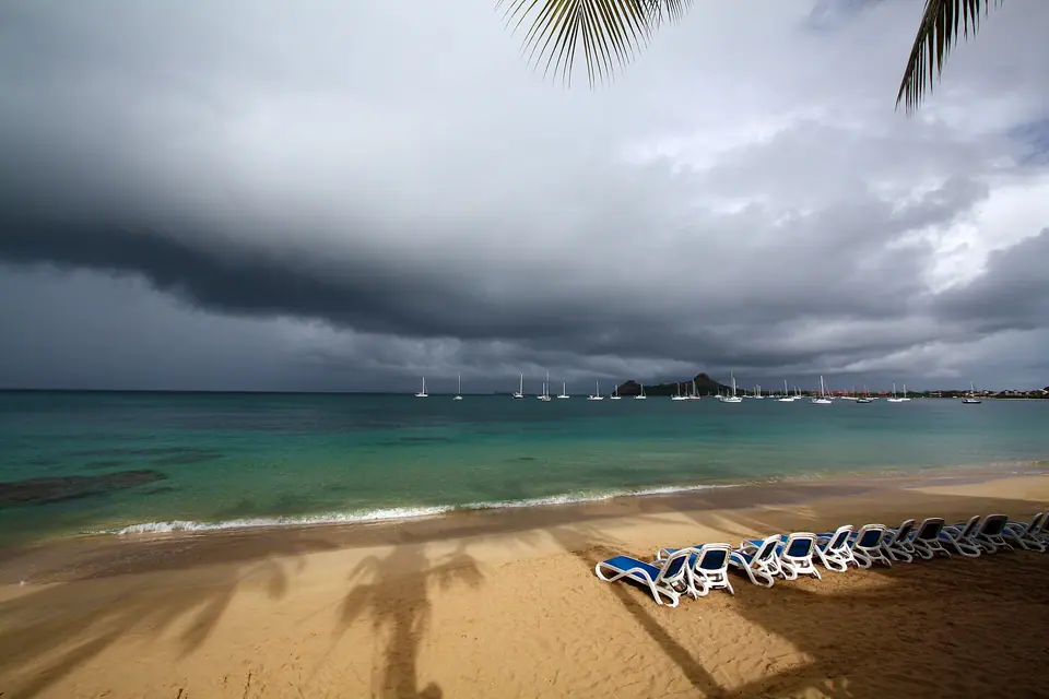 Beach loungers on golden sand at Rodney Bay under dark storm clouds with yachts moored offshore