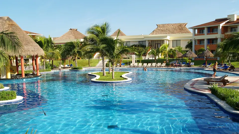 Large free-form pool with palm islands, thatched palapas and loungers in front of low resort buildings at the Bahia Principe complex in Akumal