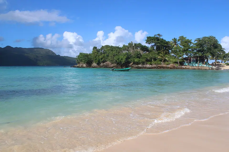 Turquoise water and pale sand at Playa Rincón on the Samaná peninsula, with a wooded headland and a small boat offshore