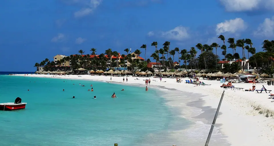 Bright white sand and shallow turquoise water on the beach between the Tamarijn and Divi resorts, with palms and low-rise buildings