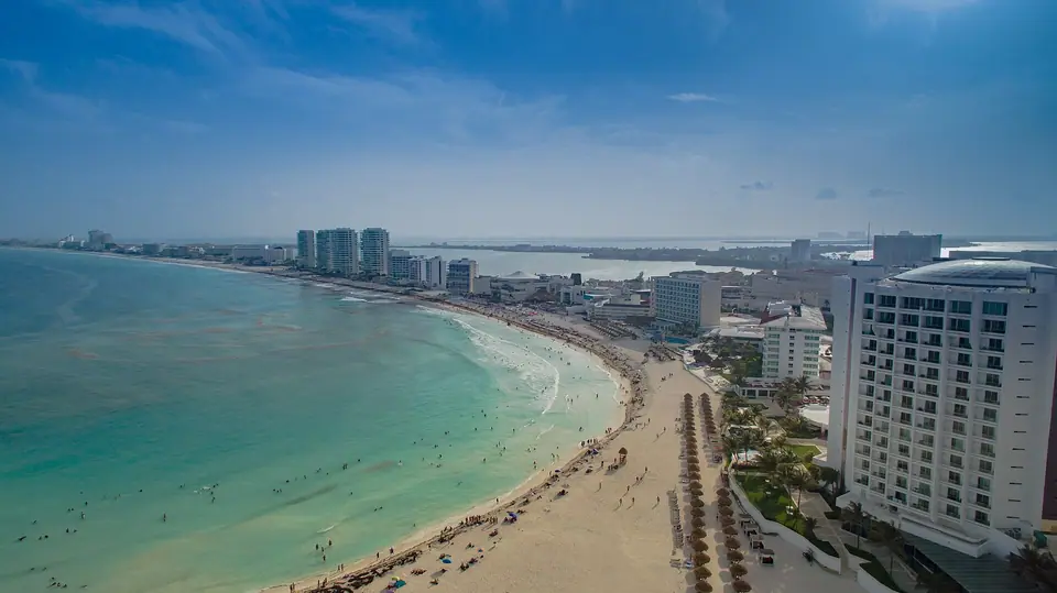 Aerial view of a long curving Cancun Hotel Zone beach with turquoise water and hotel towers along the shore