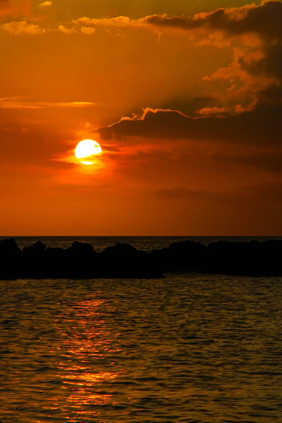 Orange sun setting over the sea and a dark breakwater at Mambo Beach, Curaçao