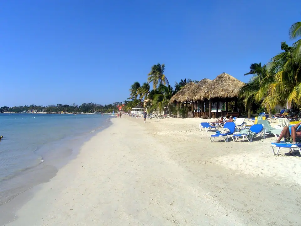 Palm trees, loungers and calm turquoise water on the beach at Sandals Negril in Jamaica