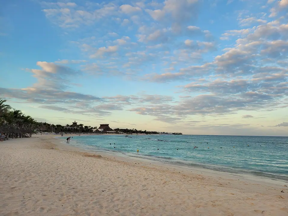 Long, empty stretch of pale sand and calm turquoise water at Playa Paraíso in Tulum under a soft evening sky