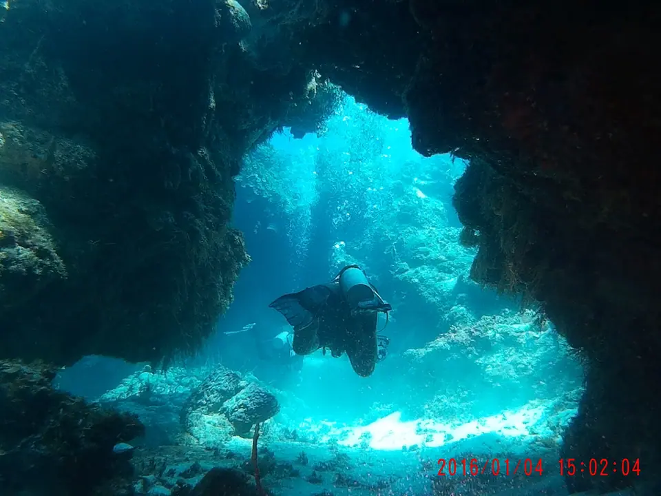 A scuba diver silhouetted inside a coral swim-through at Palancar Reef, with bright blue water beyond the opening