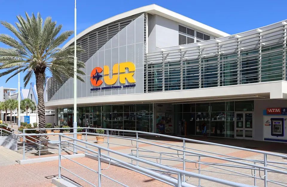 Modern white terminal building of Curaçao International Airport with large CUR letters and a palm tree in front