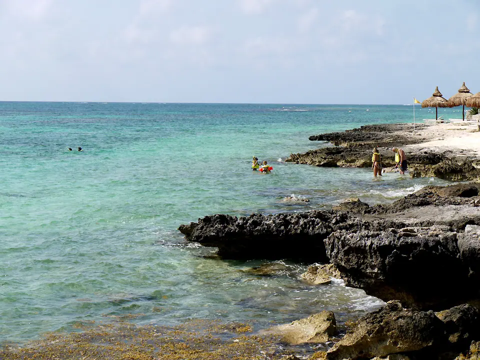 Clear turquoise water over rocks and sand at Punta Nizuc, the southern tip of Cancun's Hotel Zone, with swimmers and palapa umbrellas