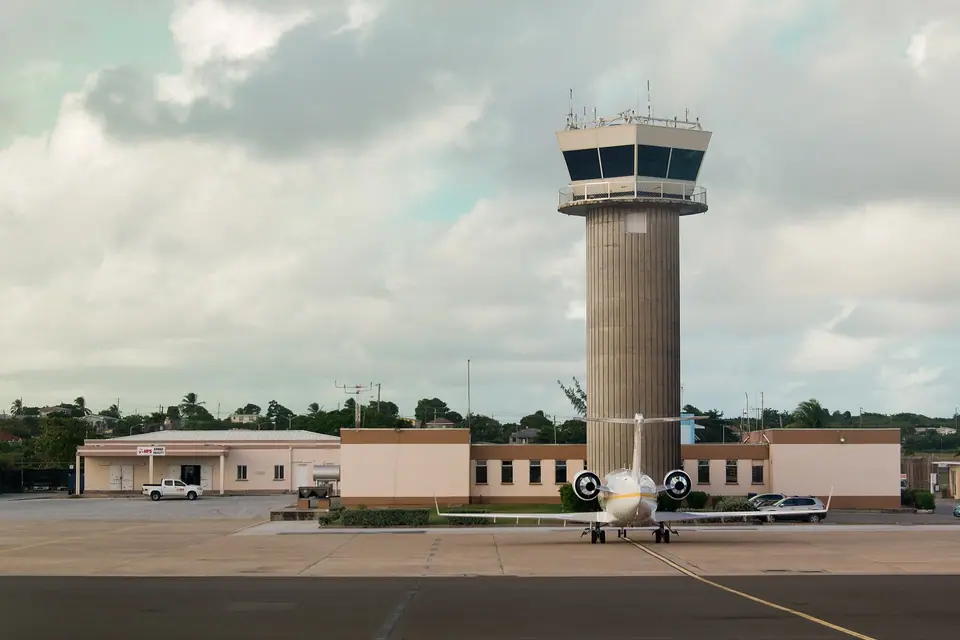 Control tower and terminal at Grantley Adams International Airport with a small jet parked on the apron