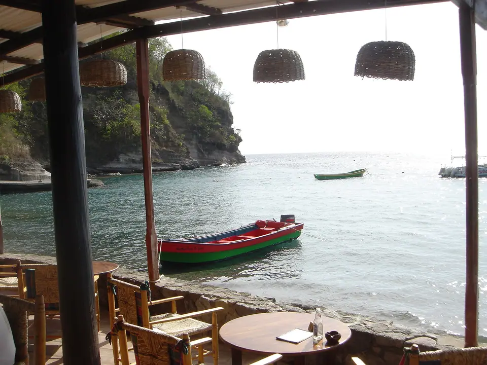 View from a waterside bar at Anse Chastanet, St. Lucia, with wicker lamps, a red fishing boat and green cliffs