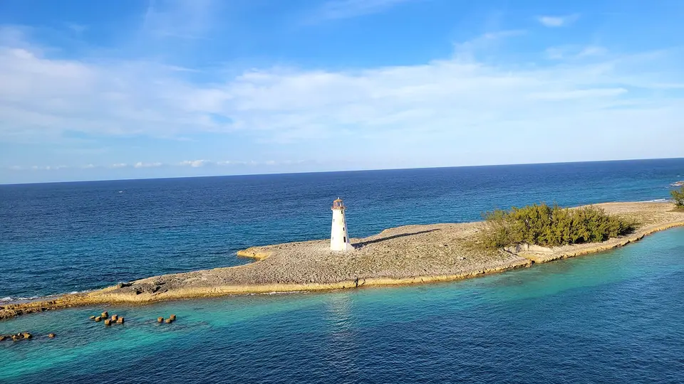Small white lighthouse on a rocky spit at the entrance to Nassau Harbour, surrounded by deep blue water