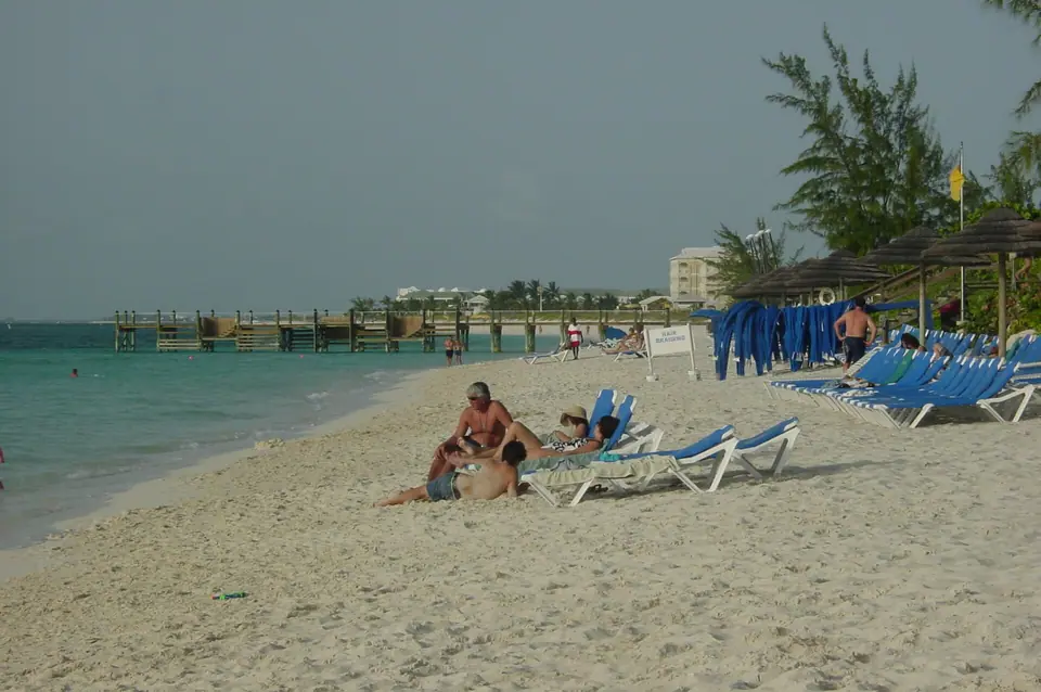 Guests on blue loungers on the white-sand beach at Beaches Turks and Caicos with a wooden pier behind