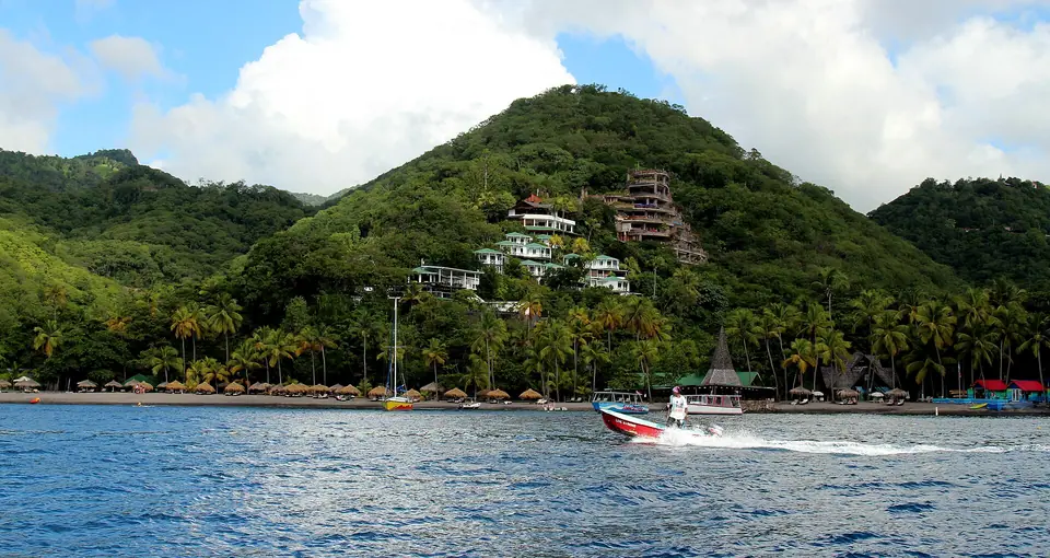 Jade Mountain's terraced stone buildings on a green hillside above Anse Chastanet bay, with a speedboat in the foreground