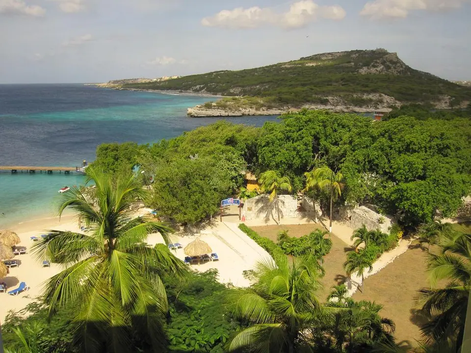 Elevated view over palm trees and a sandy cove toward Piscadera Bay and a green headland on Curaçao