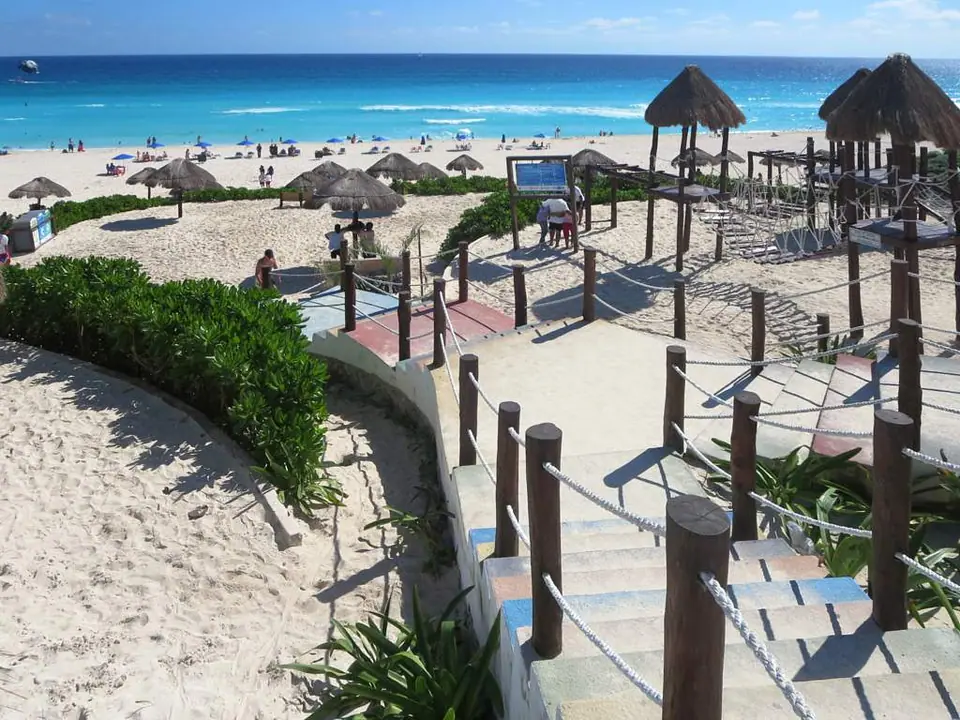 Wooden boardwalk and palapa shades leading down to the wide sand and turquoise sea at Playa Delfines in Cancun's south Hotel Zone