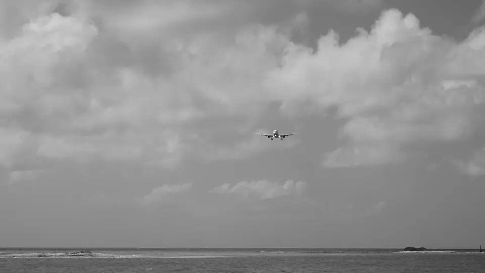 Black-and-white photo of a JetBlue jet on approach over the sea to Queen Beatrix International Airport, Aruba