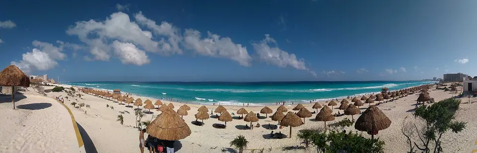 Panorama of Playa Delfines with rows of thatched palapa shades on white sand and a bright blue sea