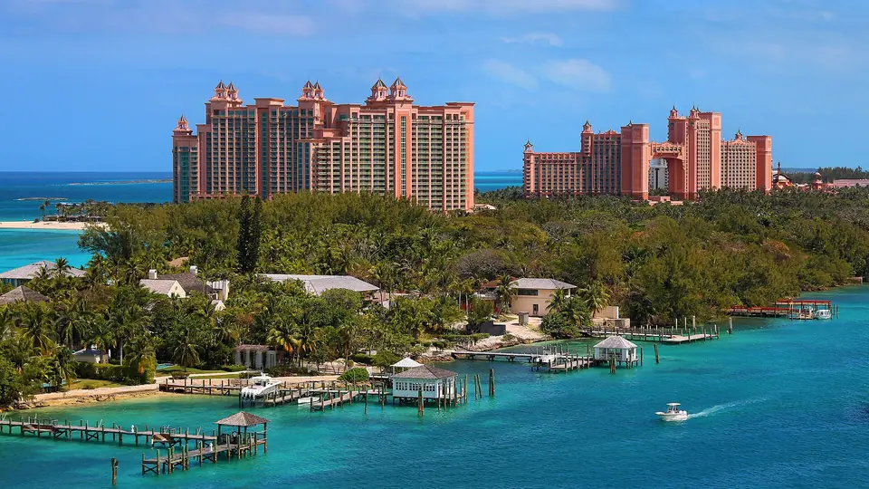 The coral-pink Royal Towers of Atlantis on Paradise Island rising above green trees, docks and turquoise harbour water