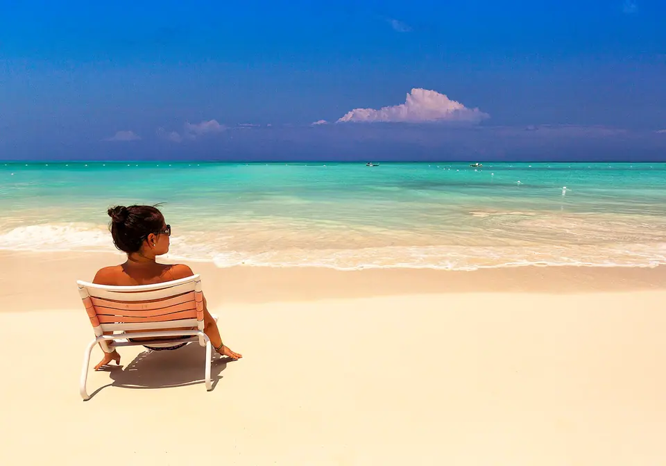 Woman relaxing on a beach chair facing the turquoise water of Grace Bay under a bright blue sky