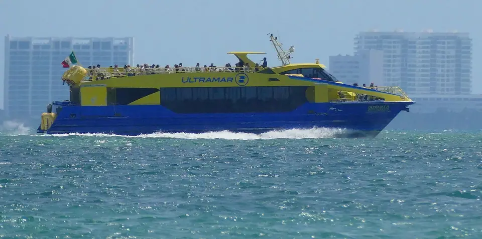 Yellow and blue fast ferry crossing the bay toward Isla Mujeres, with Cancun hotel towers in the background