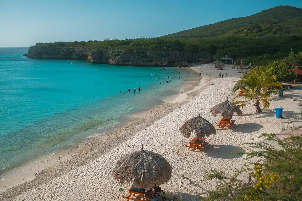 White-sand Grote Knip beach in western Curaçao with thatched sun shelters, turquoise water and a green hillside