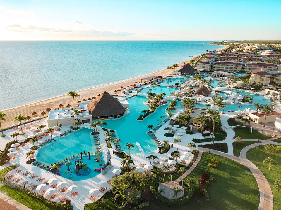 Aerial view of Moon Palace Cancun's connected blue pools, thatched palapas and loungers running down to a long beach