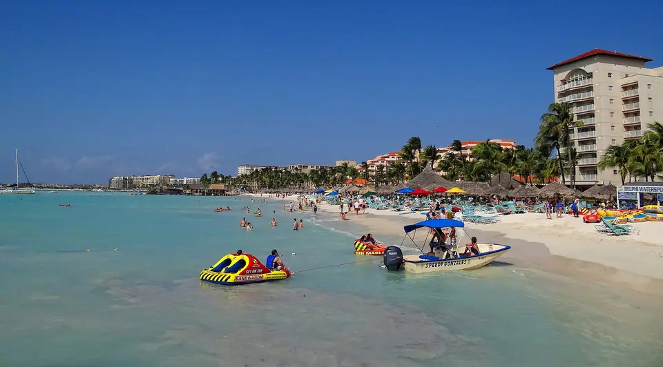 Swimmers, inflatable rides and small boats in calm turquoise water off Palm Beach, Aruba, with high-rise hotels behind the sand