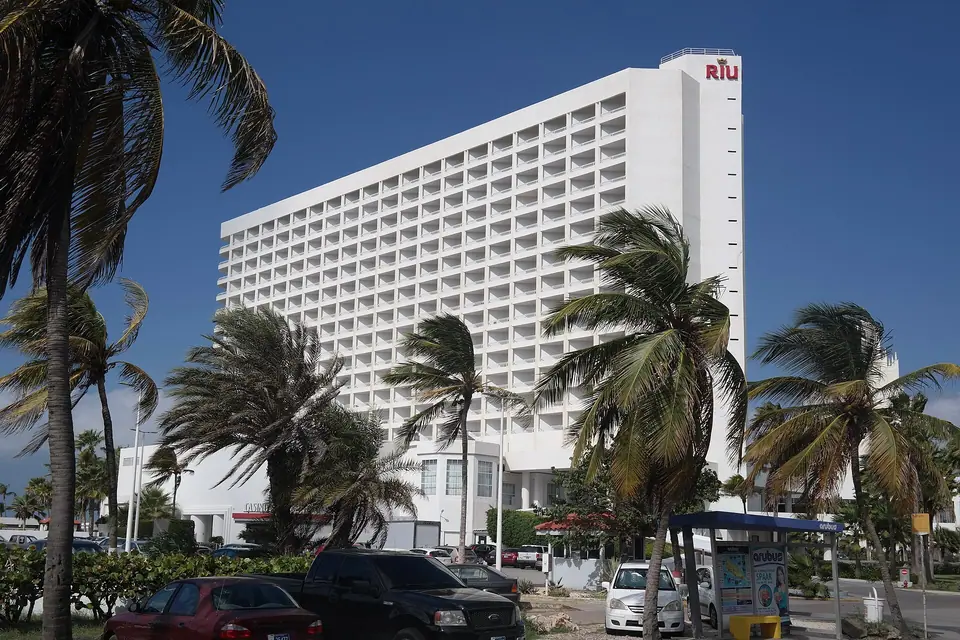 White high-rise tower of Hotel Riu Palace Aruba with its RIU sign, framed by palm trees under a deep blue sky