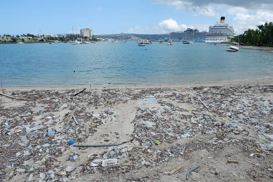 Public beach near Montego Bay's cruise port covered in storm debris and plastic, with cruise ships and moored boats behind