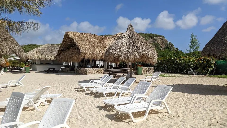 White sun loungers and thatched huts on the sand at Cas Abao beach, Curaçao, under a blue sky