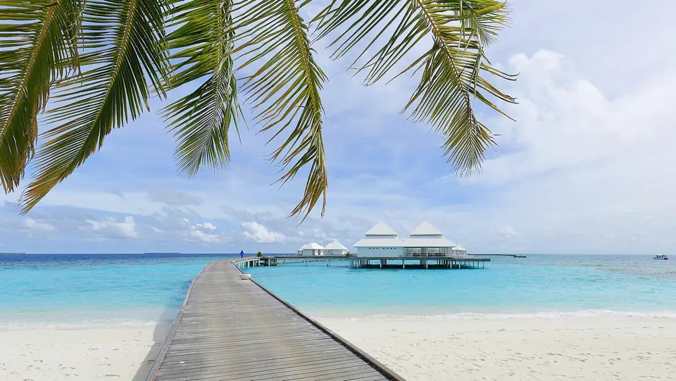 Wooden walkway leading out to overwater villas above a clear lagoon in Ari Atoll